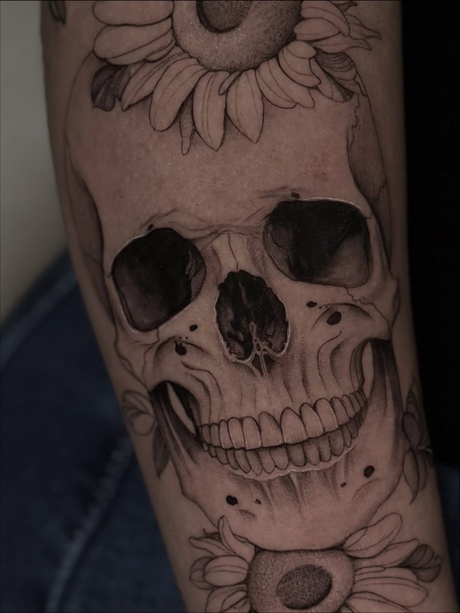 Skull framed by sunflowers, black and grey realism tattoo on a forearm
