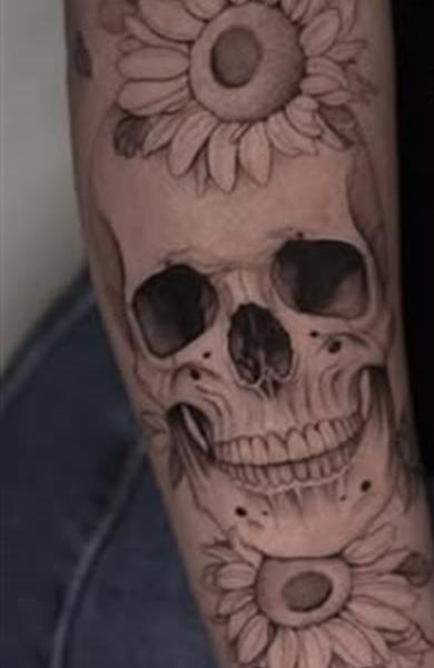 Skull framed by sunflowers, black and grey realism tattoo on a forearm
