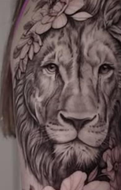 Lion crowned with flowers, black and grey realism tattoo on an upper arm